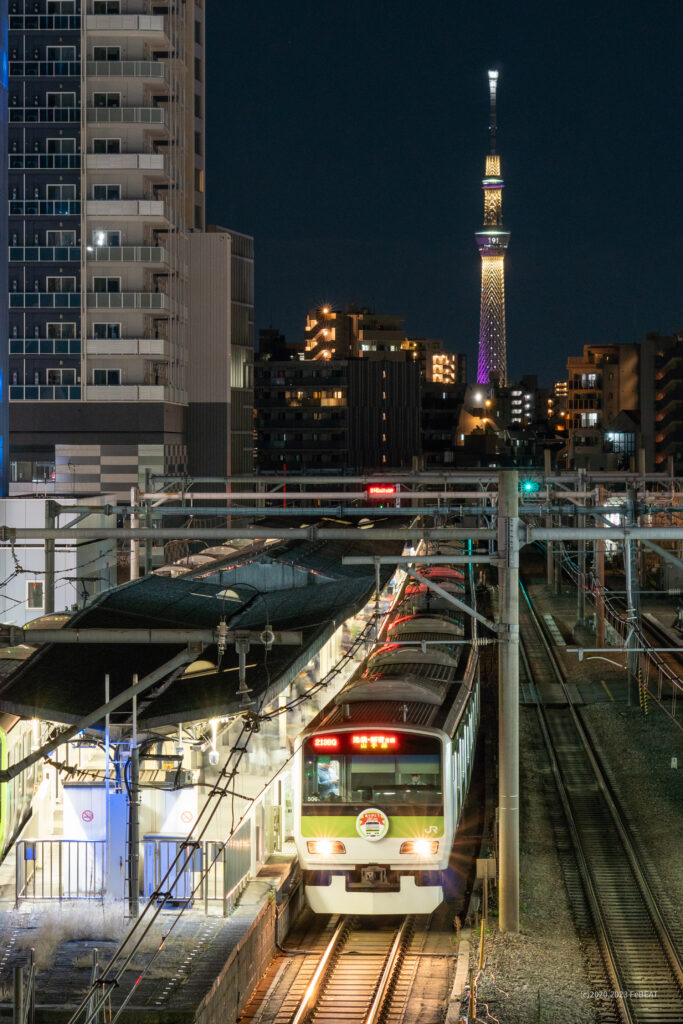 スカイツリーの夜景を背に山手線の大塚駅に停車するE231系
